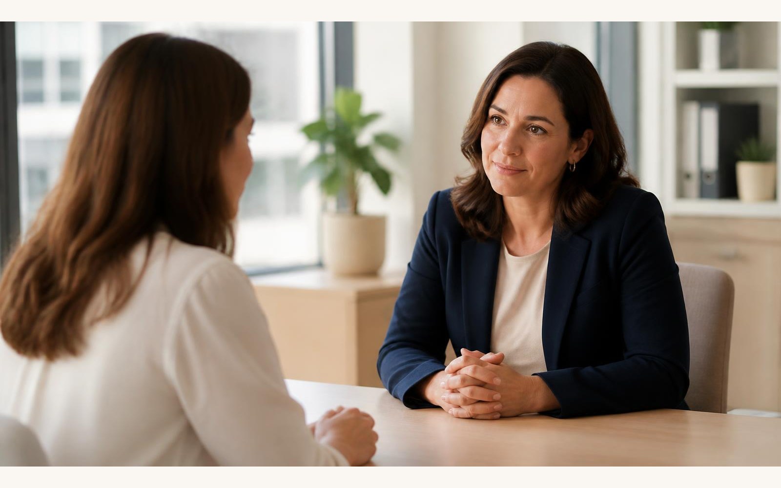 An HR leader in a navy blazer having a supportive one-on-one career transition conversation with an employee in a bright modern office